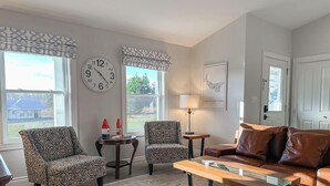 A living room with patterned armchairs, a glass-top coffee table, a brown leather sofa, a wall clock, and a framed map. - Home Away Villa: Ideal for Island Adventures (Stanley Bridge)