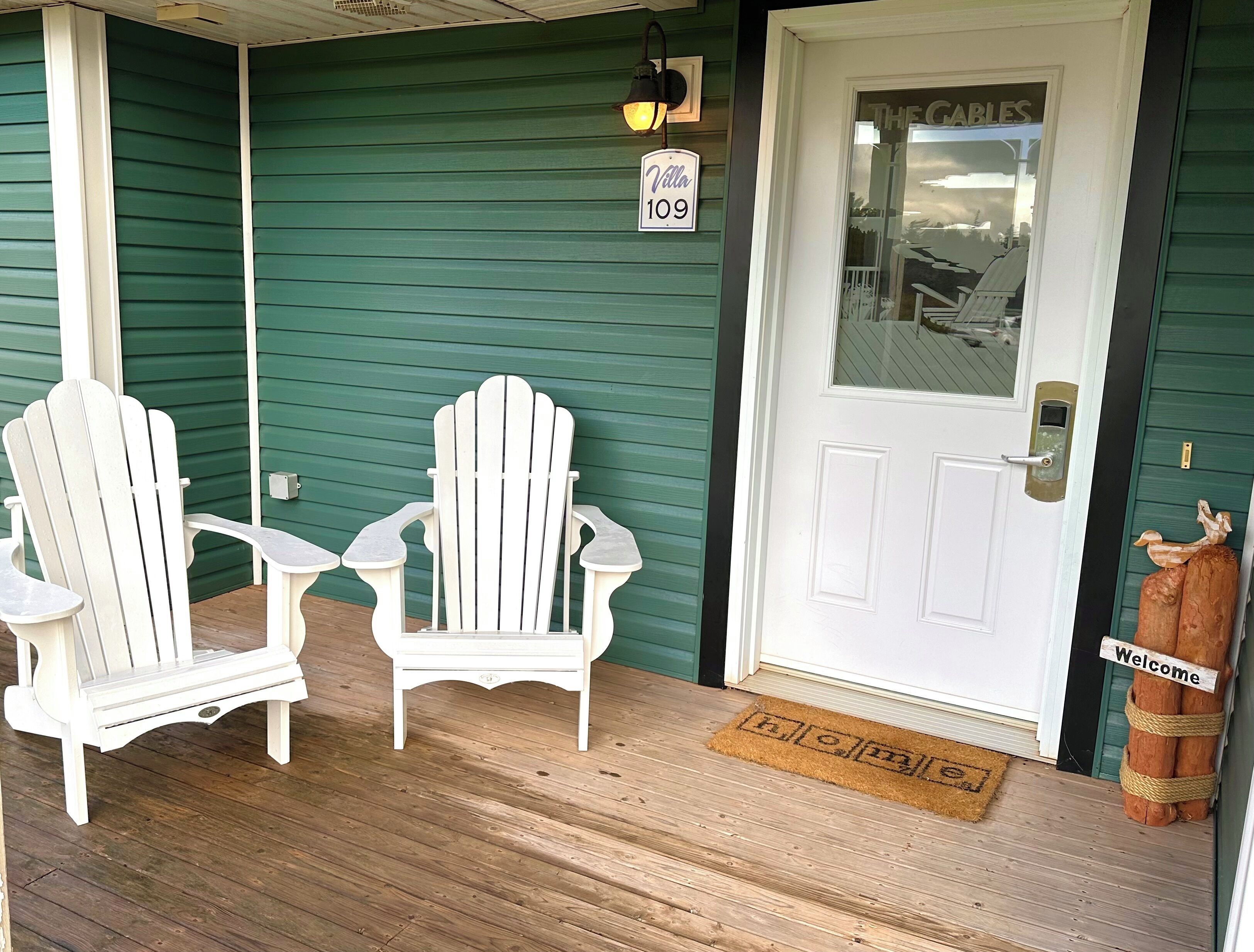 A porch with two white Adirondack chairs, a door labeled 'The Cables,' and a welcome sign.