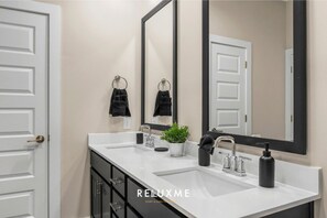 A modern bathroom with two sinks, a large mirror, and a potted plant. - Reluxme|Uptown 2BR w/ Hot Tub, Gym, Pools & Views (Charlotte)