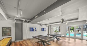 Un espace piscine intérieur moderne, doté d’une table de billard, de chaises longues et offrant une vue sur la piscine extérieure.