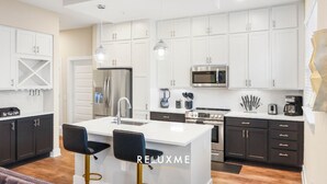A modern kitchen with white cabinets, stainless steel appliances, and pendant lighting.