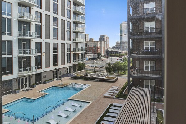 Un immeuble d’appartements moderne doté d’un espace piscine sur le toit, comprenant une piscine et des chaises longues.