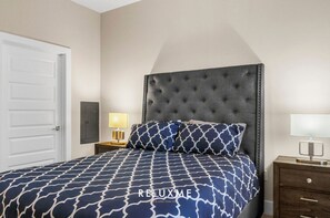 A bedroom with a tufted headboard, a patterned bedspread, two bedside lamps, and a wooden nightstand. - Reluxme|Uptown 2BR w/ Hot Tub, Gym, Pools & Views (Charlotte)