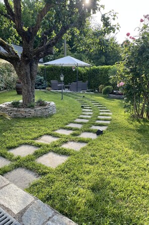 A garden with a stone pathway, a tree, and outdoor furniture under a gazebo. - Bellavista by Interhome (Acqui Terme)