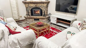 A cozy living room with a stone fireplace, a flat-screen TV, and a comfortable seating area with a red patterned rug. - Bellavista by Interhome (Acqui Terme)