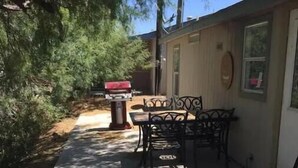 A patio area with a table and chairs, a barbecue grill, and a small trash can. - River House (Parker)