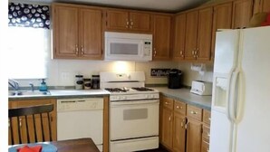 A kitchen with wooden cabinets, a white stove, a microwave, and a refrigerator. - River House (Parker)