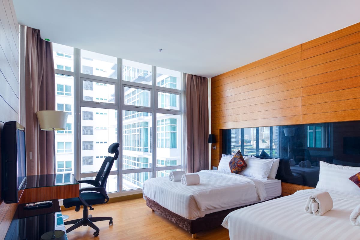 Une chambre d’hôtel avec deux lits, un bureau, une chaise et de grandes fenêtres donnant sur la ville.