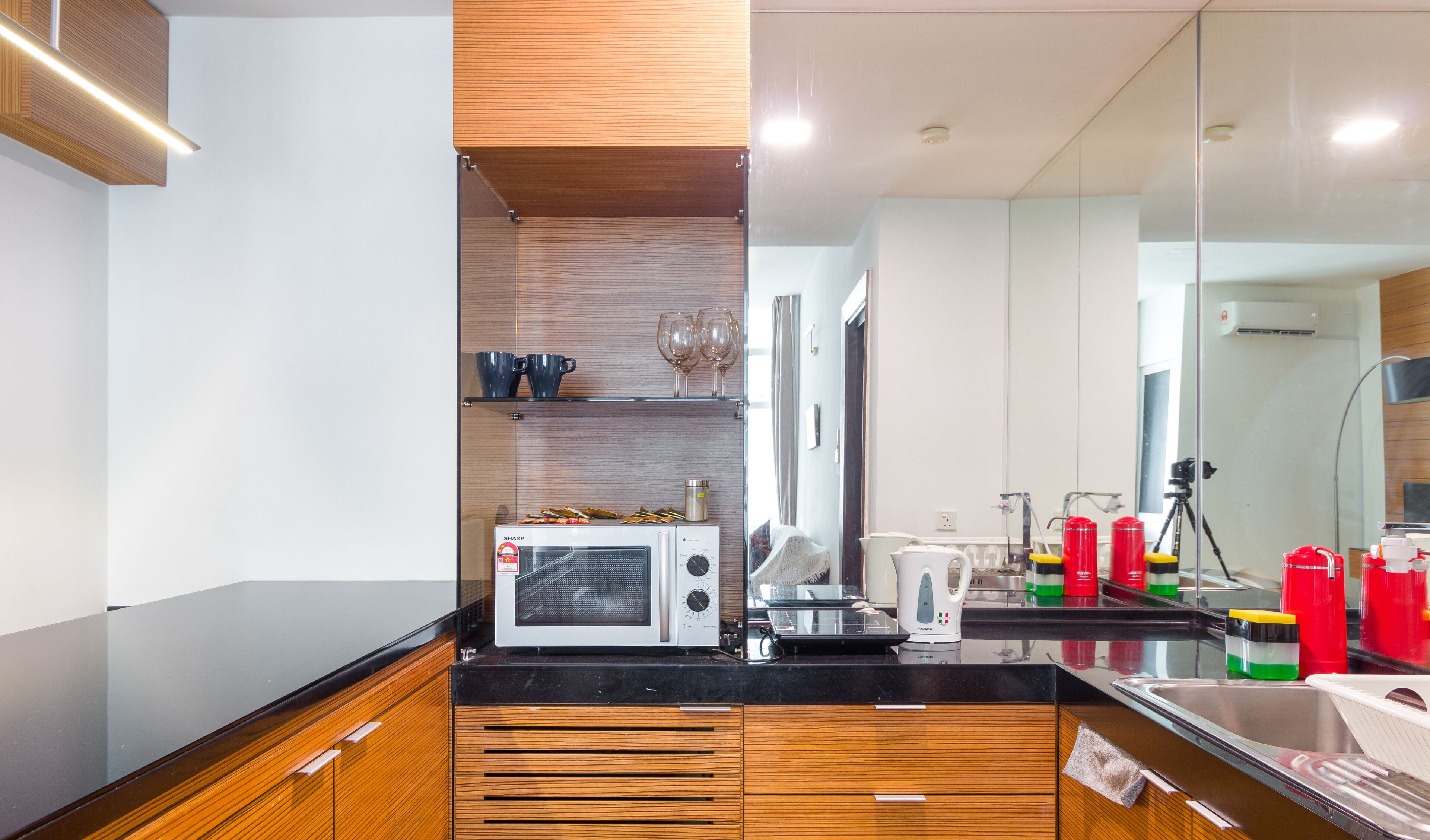 A modern kitchen with wooden cabinetry, a microwave, a kettle, and a coffee machine.