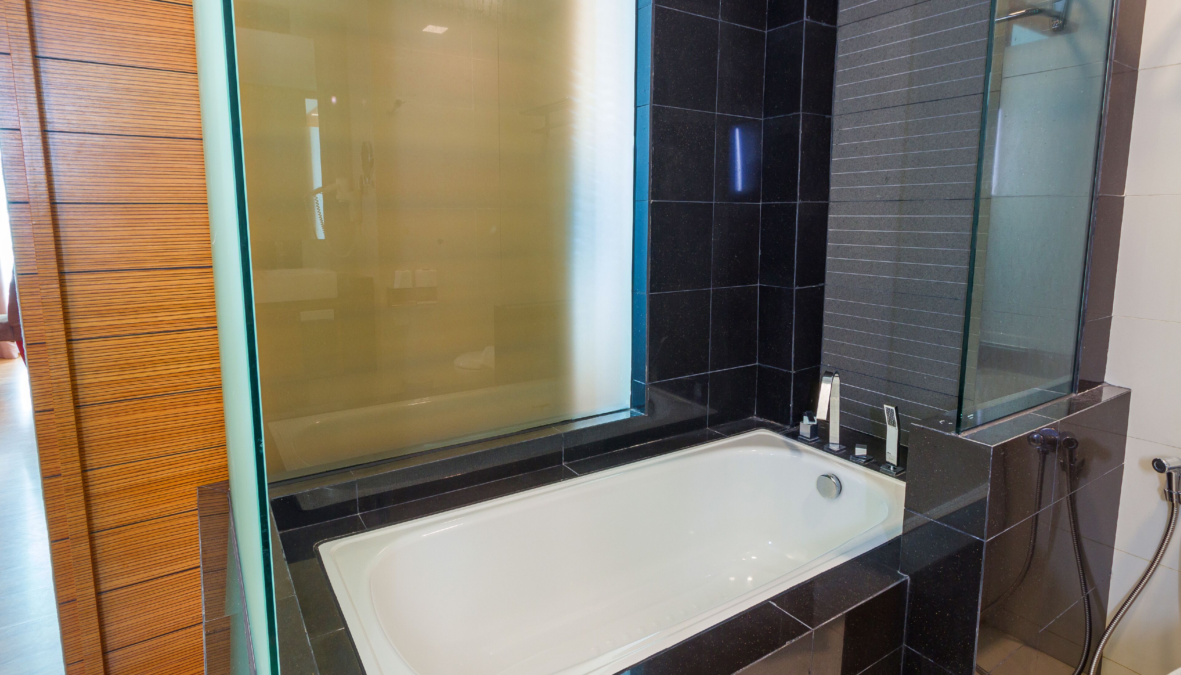 Ein modernes Badezimmer mit Duschkabine aus Glas, einer weißen Badewanne und schwarzen Fliesenwänden.