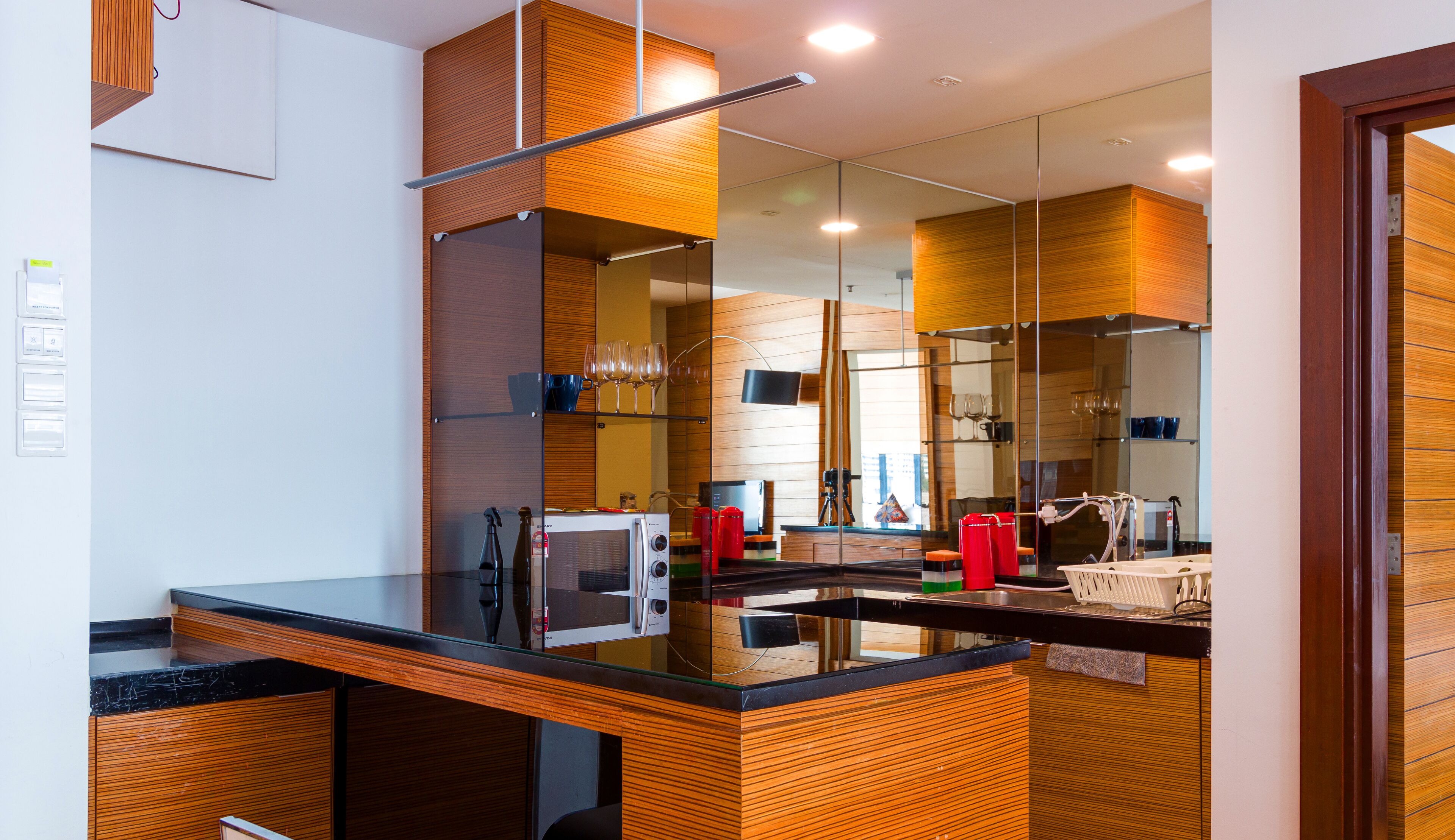 Una cocina moderna con encimera de vidrio, armarios de madera y un espejo grande que refleja el ambiente.