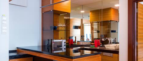 Una cocina moderna con encimera de vidrio, armarios de madera y un espejo grande que refleja el ambiente.