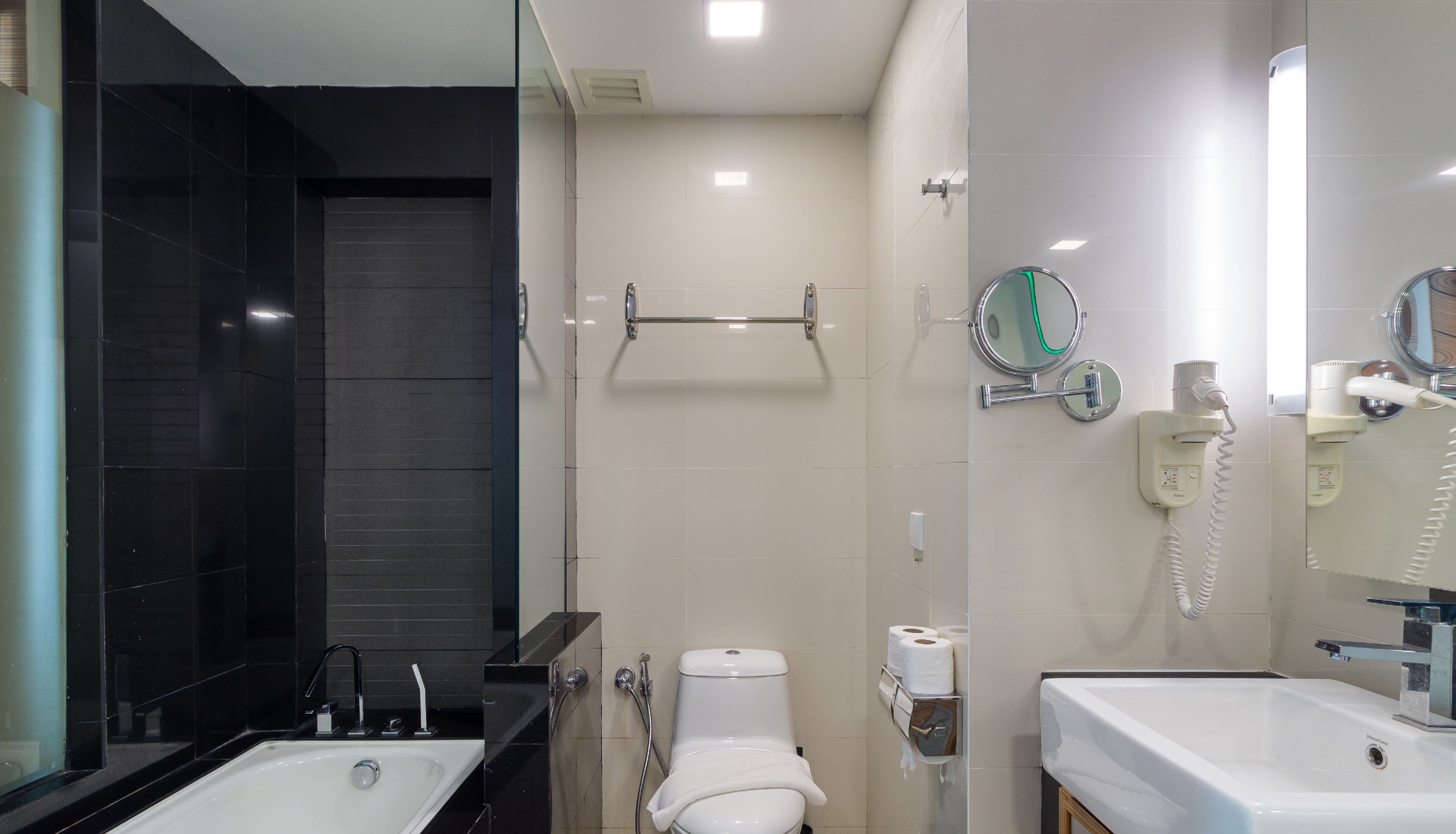 A modern bathroom with a glass-enclosed shower, a toilet with a towel rack, and a vanity with a mirror.