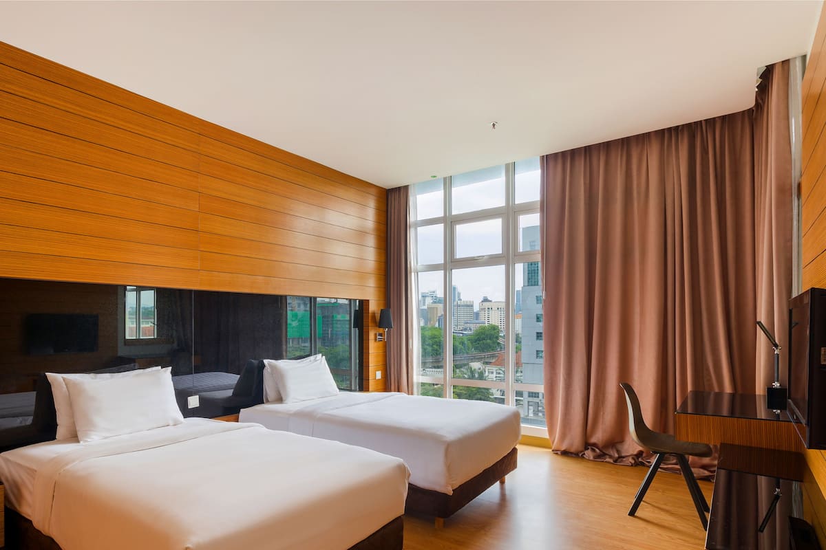 Une chambre d’hôtel avec deux lits, une grande fenêtre avec des rideaux, un téléviseur fixé au mur et un plafond en bois.