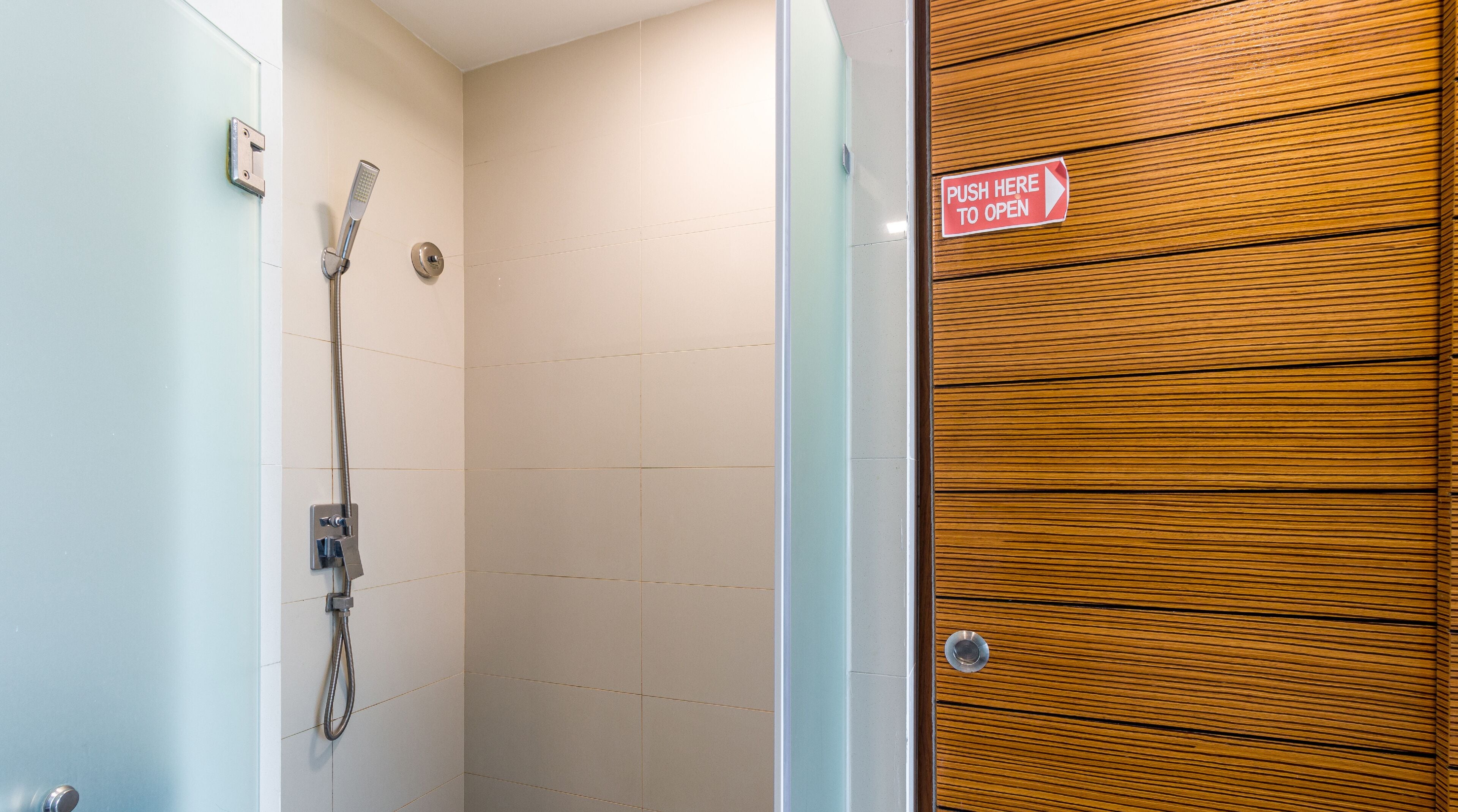 A shower with a handheld showerhead and a push-to-open door.