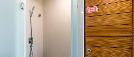A shower with a handheld showerhead and a push-to-open door.