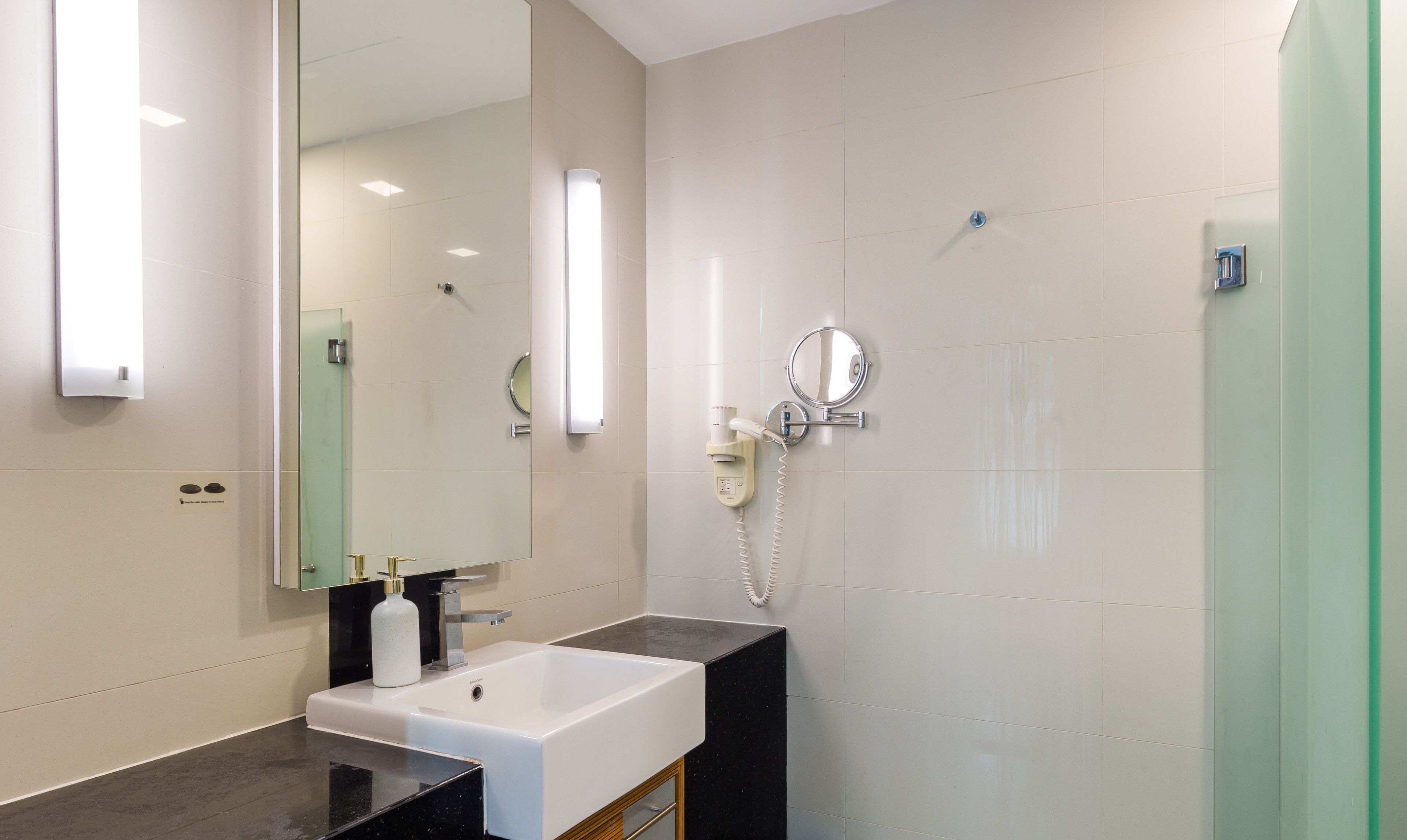 Un baño moderno con un espejo grande, un lavamanos blanco, un cabezal de ducha manual y una ducha con cerramiento de vidrio.