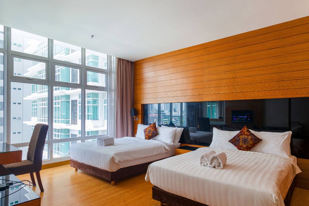 Une chambre d’hôtel avec deux lits, un bureau et une grande fenêtre donnant sur la ville.