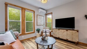 Een moderne woonkamer met grote ramen, een flatscreen televisie, een ronde salontafel en een leren bank.