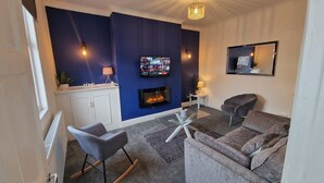 A living room with a fireplace, a television mounted on the wall, a sofa, and a chair. - 2-Bed Home - Sleeps 4, Parking & Garden (Darlington)
