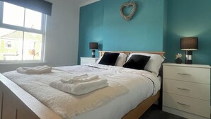 A neatly made bed with white linens and towels, a wooden headboard, and a teal accent wall. - 2-Bed Home - Sleeps 4, Parking & Garden (Darlington)