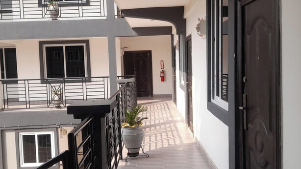 A corridor with a potted plant, a fire extinguisher, and a door. - Kasoa Apartment with 2 Bedrooms (KASOA)