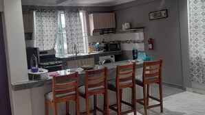 A compact kitchen with a dining area, featuring a microwave, stove, and a small island with bar stools. - Kasoa Apartment with 2 Bedrooms (KASOA)