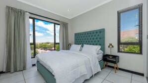 A bedroom with a large bed, a view of the outdoors, and a window with blinds. - 2 Bed Flat - Sleeps 4 - Pool - Garden - Parking (Sandton)