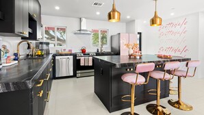 A modern kitchen with black cabinetry, a central island with bar stools, stainless steel appliances, and pendant lighting.