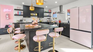 A modern kitchen with a central island, bar stools, and pink appliances.