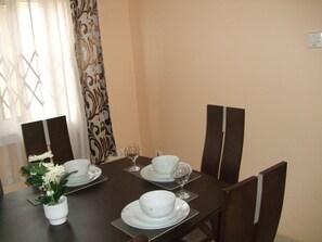 A dining table set with white plates, bowls, and wine glasses, surrounded by dark chairs.