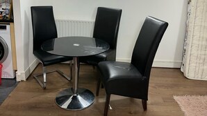 A dining area with a round table and four black chairs, a wall clock, and a radiator. - Captivating 1-Bed Apartment in London (London)