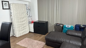 A living room with a black leather sofa, a small black cabinet, a floral bedspread, a pink rug, and a window with closed curtains. - Captivating 1-Bed Apartment in London (London)
