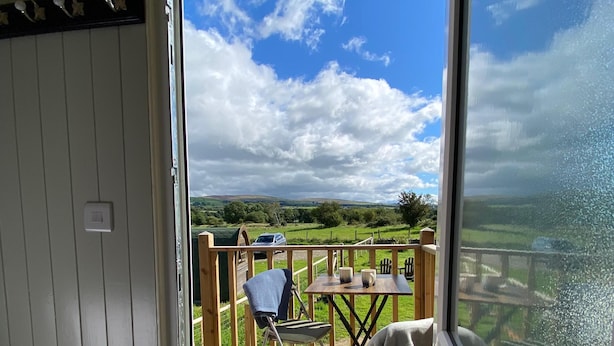 A deck with a table and chairs, a dog, and a view of a green landscape. - 1 Bed Shepherds Hut-Sleeps 2-Pets-Parking-Mtn View (Omagh)