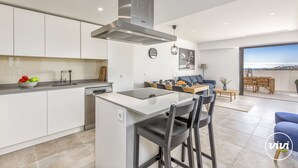A modern kitchen with a central island, dining area with a table and chairs, and a living room with a sofa and a view of the city. - Sara | Sea view - pool - terrace (La Cala de Mijas)