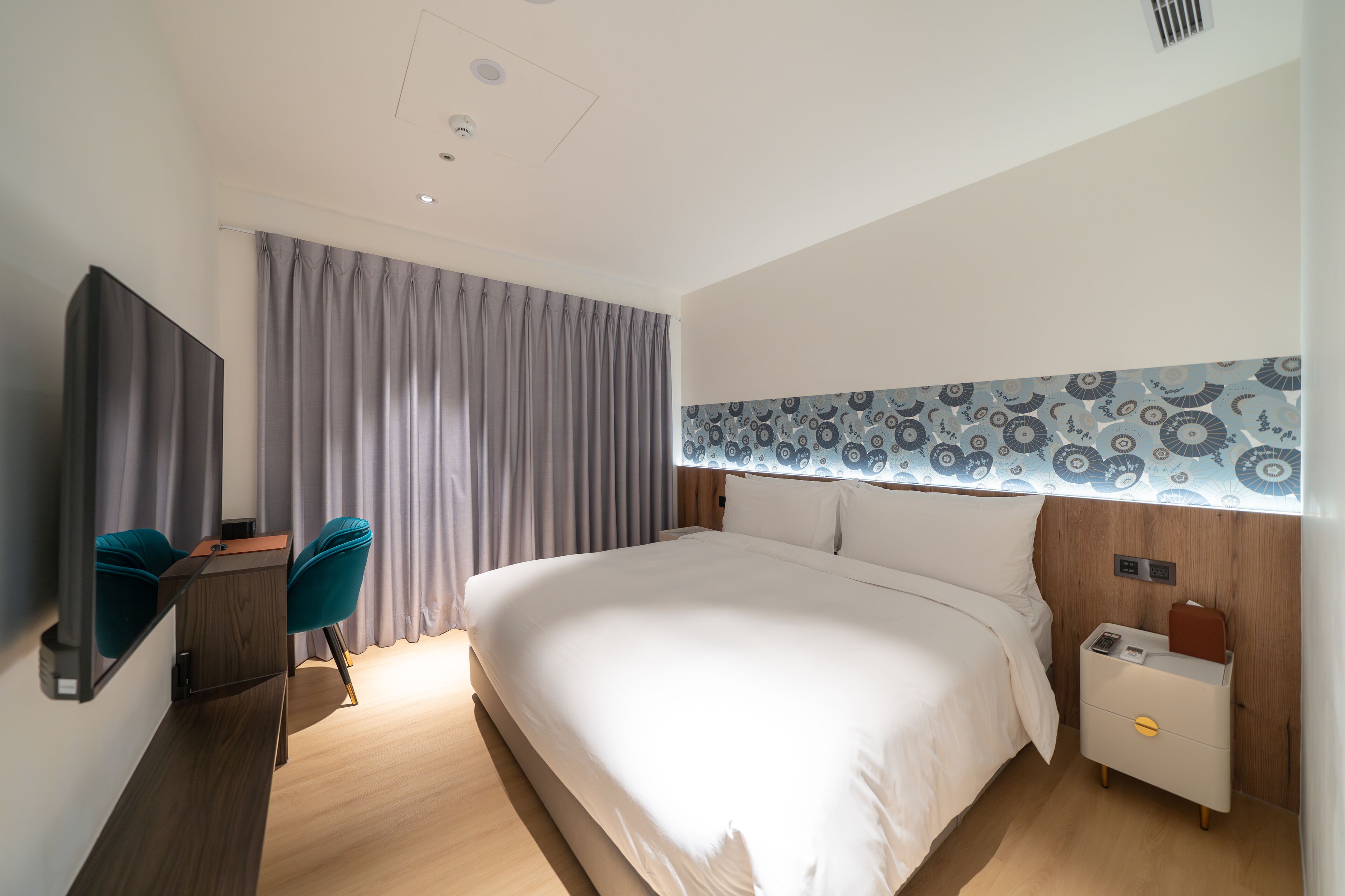 Et moderne hotelværelse med en stor seng, et skrivebord med stol og et natbord med lampe.