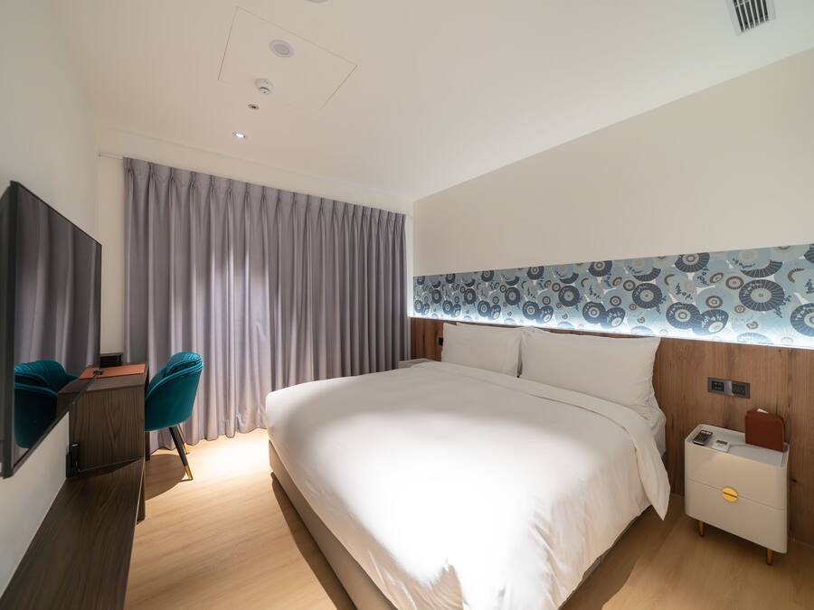 Et moderne hotelværelse med en stor seng, et skrivebord med stol og et natbord med lampe.