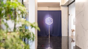 A modern interior with a reflective black floor, a blue curtain with a geometric logo, and a potted plant in the foreground. - Kashotsu Bettei (Taichung)
