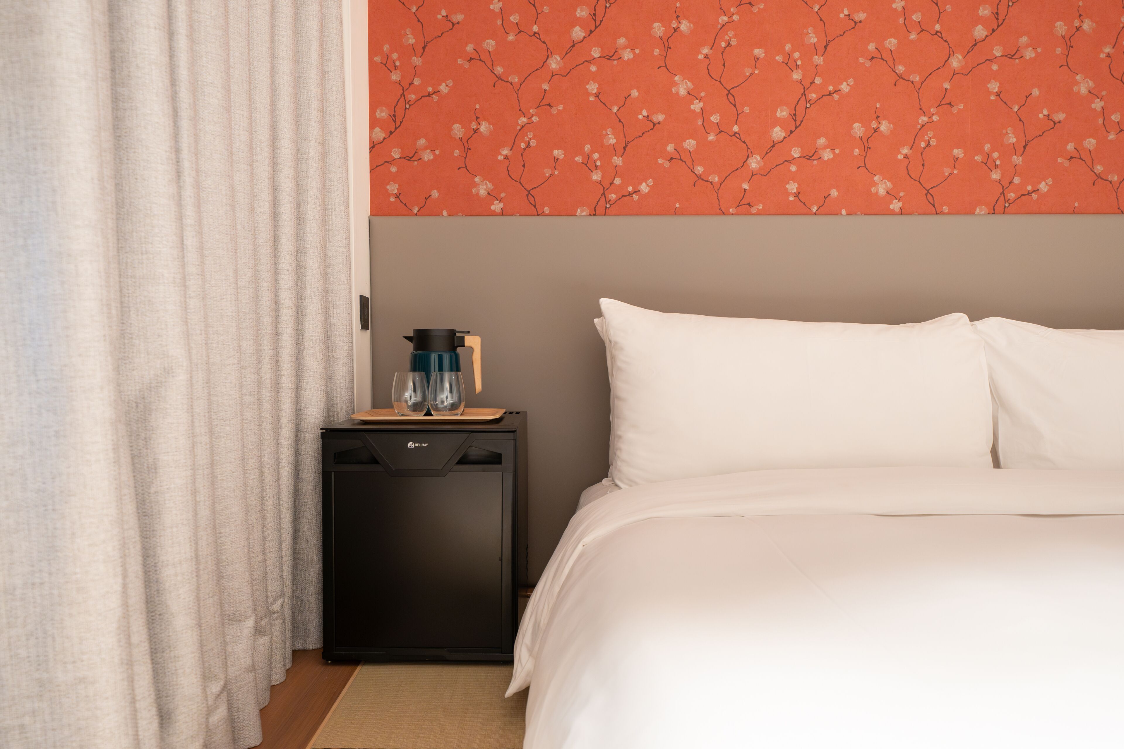 Une chambre d’hôtel avec un lit, une table de chevet, une machine à café et un mur orné d’un motif floral.