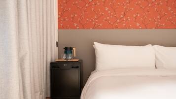 Une chambre d’hôtel avec un lit, une table de chevet, une machine à café et un mur orné d’un motif floral.