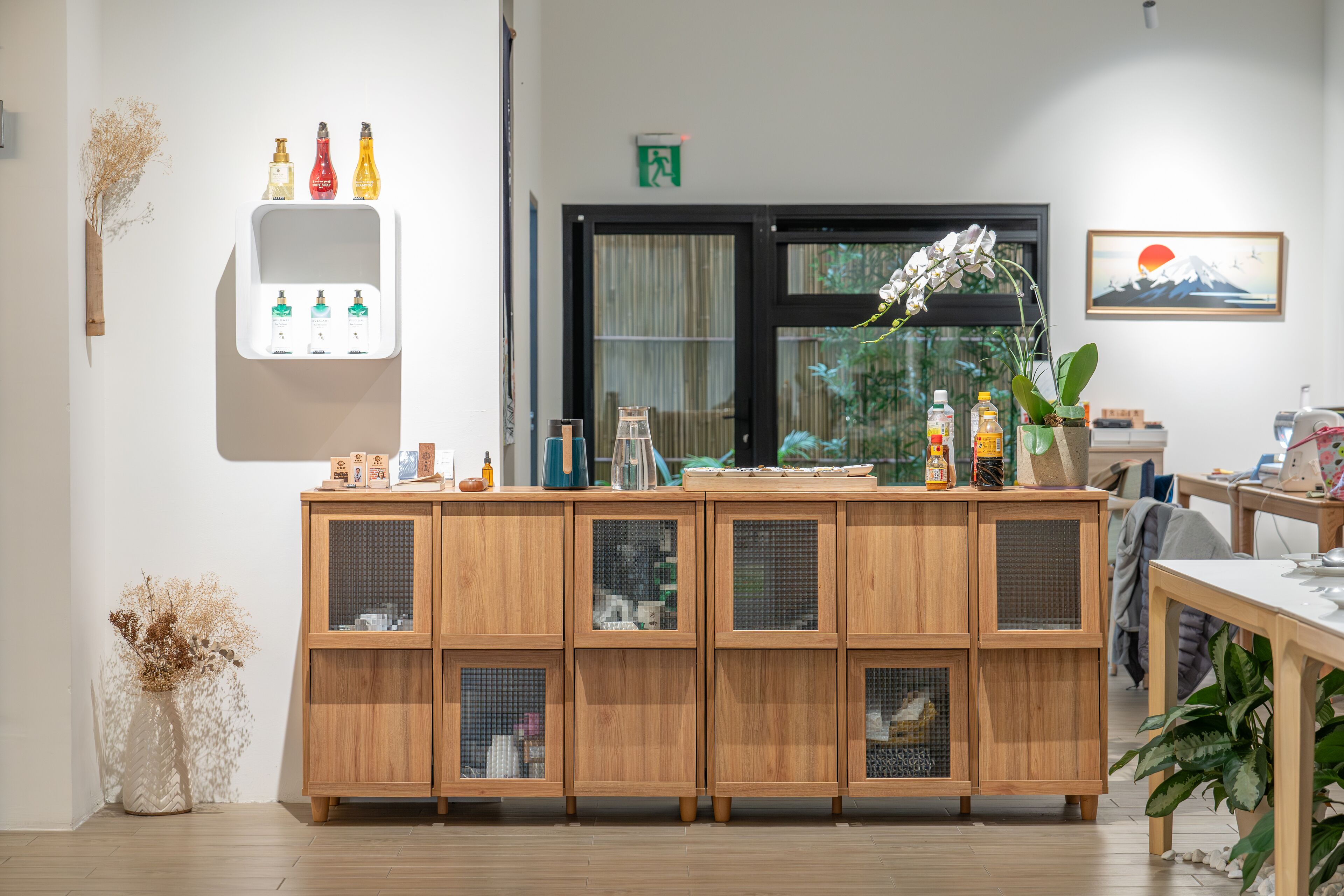 A wooden cabinet with glass doors, a shelf with bottles, and a painting of a mountain and sun.