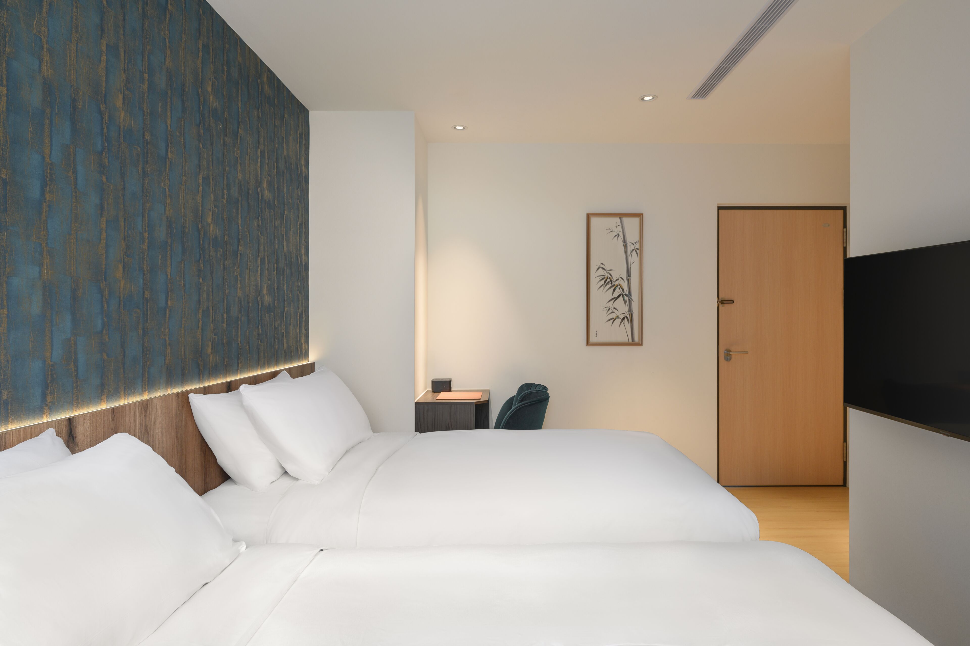 A modern hotel room with a large bed, a flat-screen TV, a wooden headboard, a nightstand, and a framed artwork on the wall.