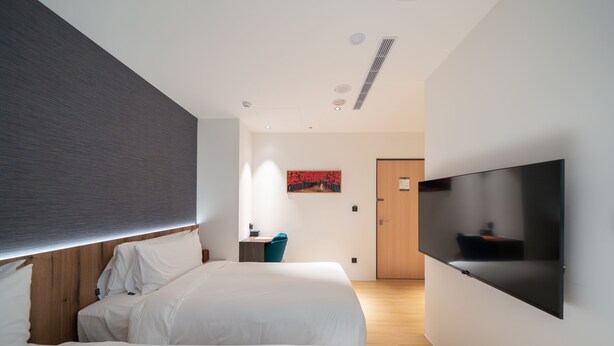 A modern hotel room with two beds, a flat-screen TV mounted on the wall, and a wooden door in the background. - Kashotsu Bettei (Taichung)