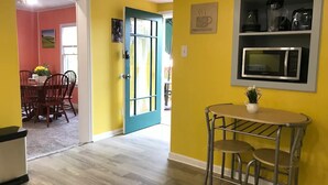 A bright yellow room with a teal door, a small metal table with two stools, and a microwave on the wall. - Spacious 3 Bedroom in Downtown Danville: Welcome to 4th Street Retreat (Danville)