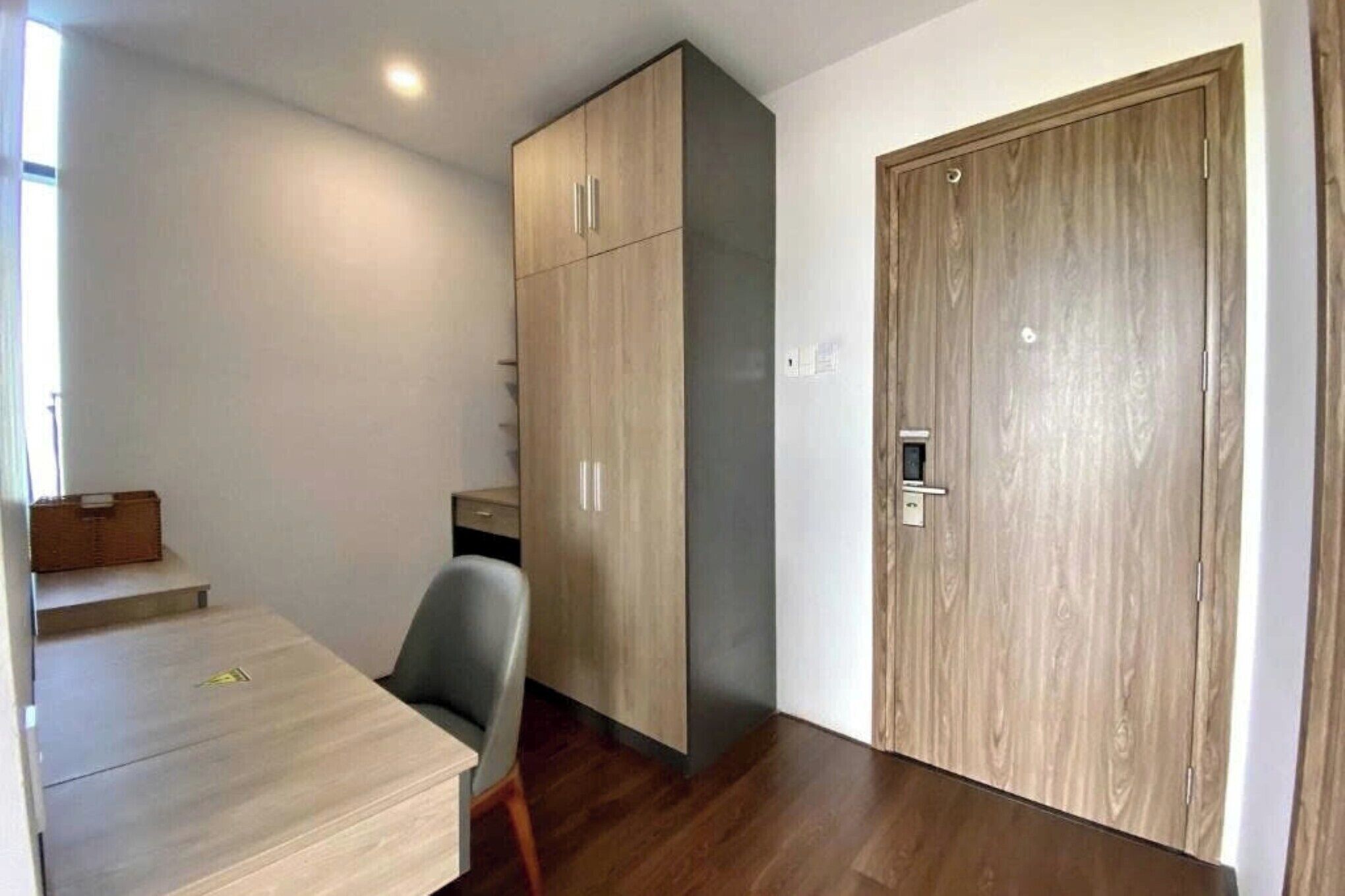 Habitació petita i moderna amb un armari de fusta, una taula i una cadira.