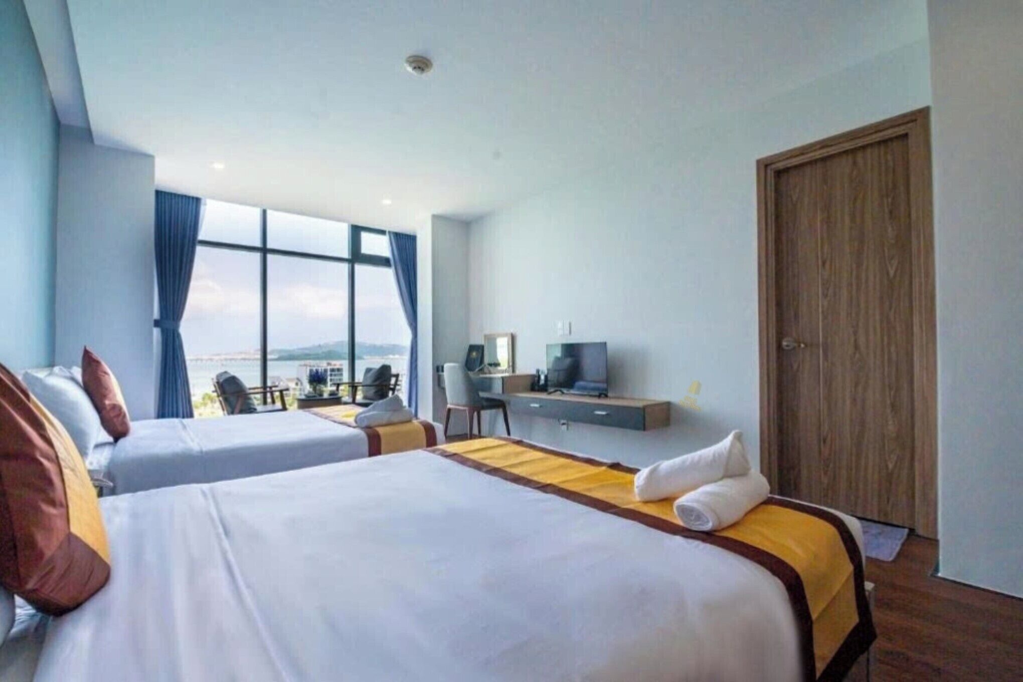 Une chambre d’hôtel avec deux lits, un bureau, une télévision et une grande fenêtre donnant sur un beau paysage.