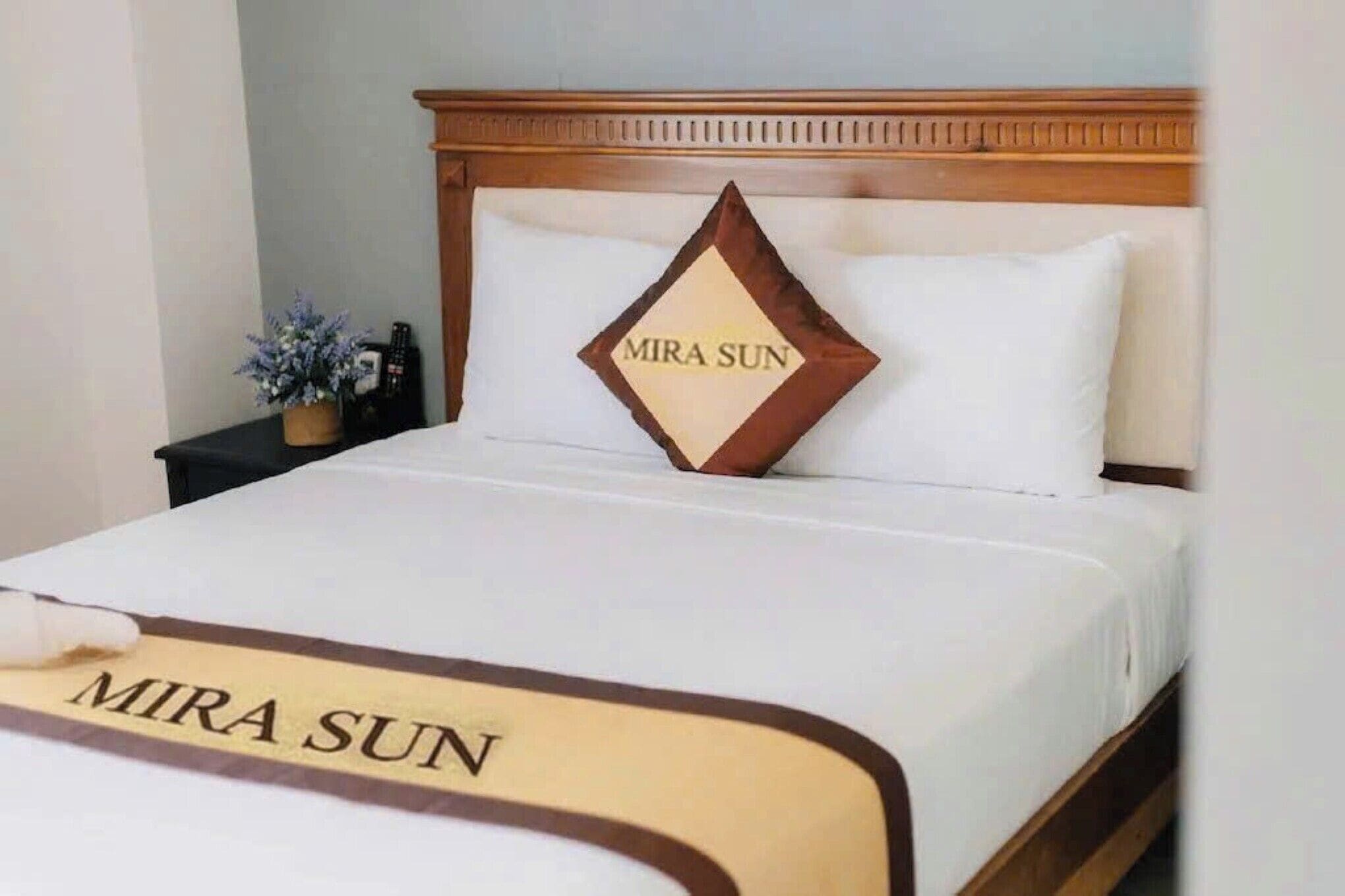 A neatly made bed with a pillow labeled "MIRA SUN" and a bedspread with the same text.