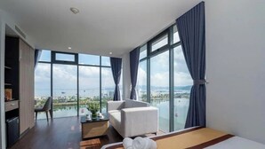 Ein modernes Hotelzimmer mit einem großen Bett, einer Sitzecke und Blick auf eine Stadtlandschaft durch große Fenster.
