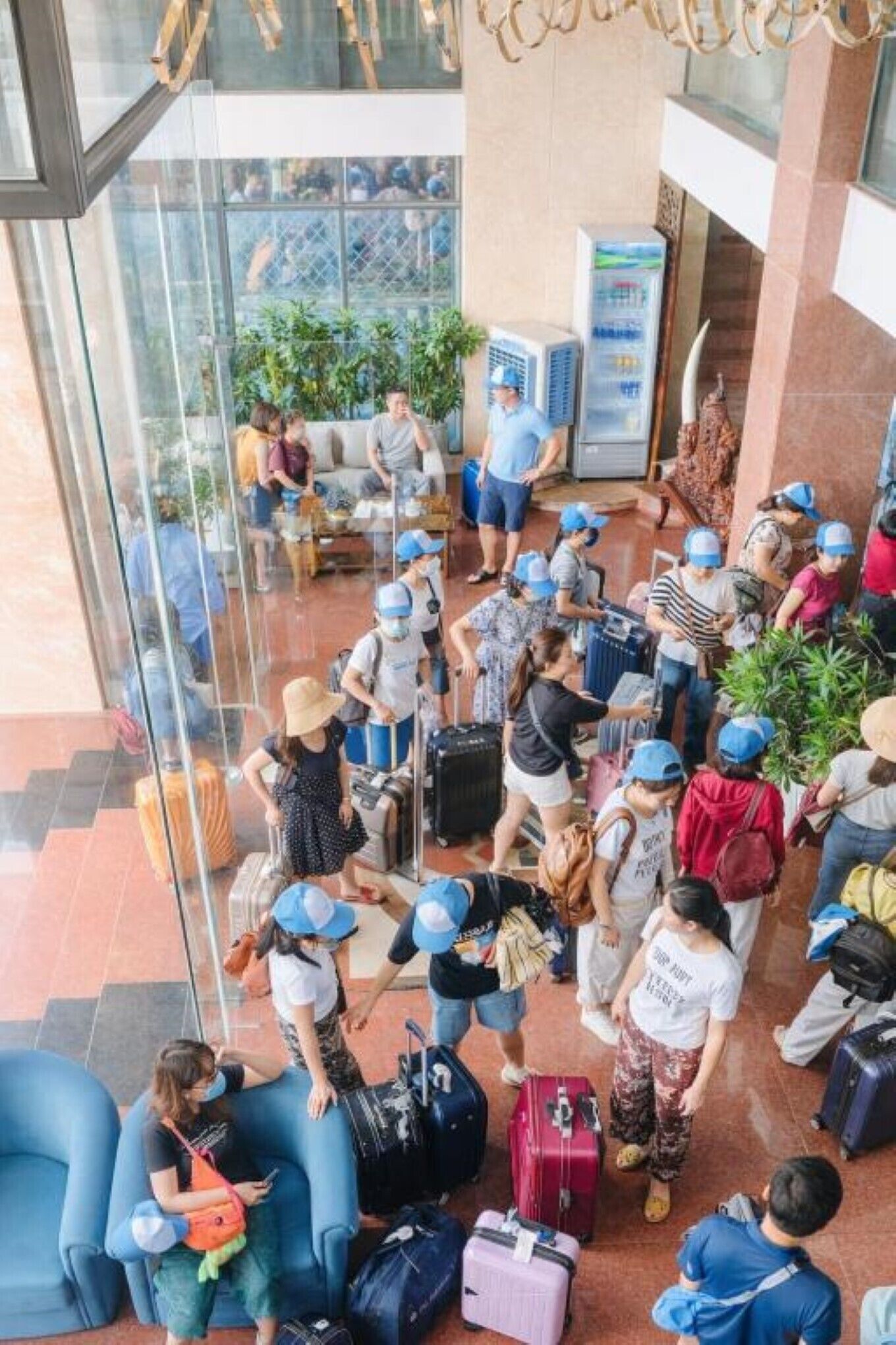 A group of people with luggage in a lobby area with seating and a glass wall.