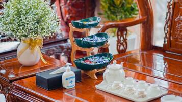 A wooden table with a vase of white flowers, a bowl of snacks, a bottle of hand sanitizer, and a tray of condiments.